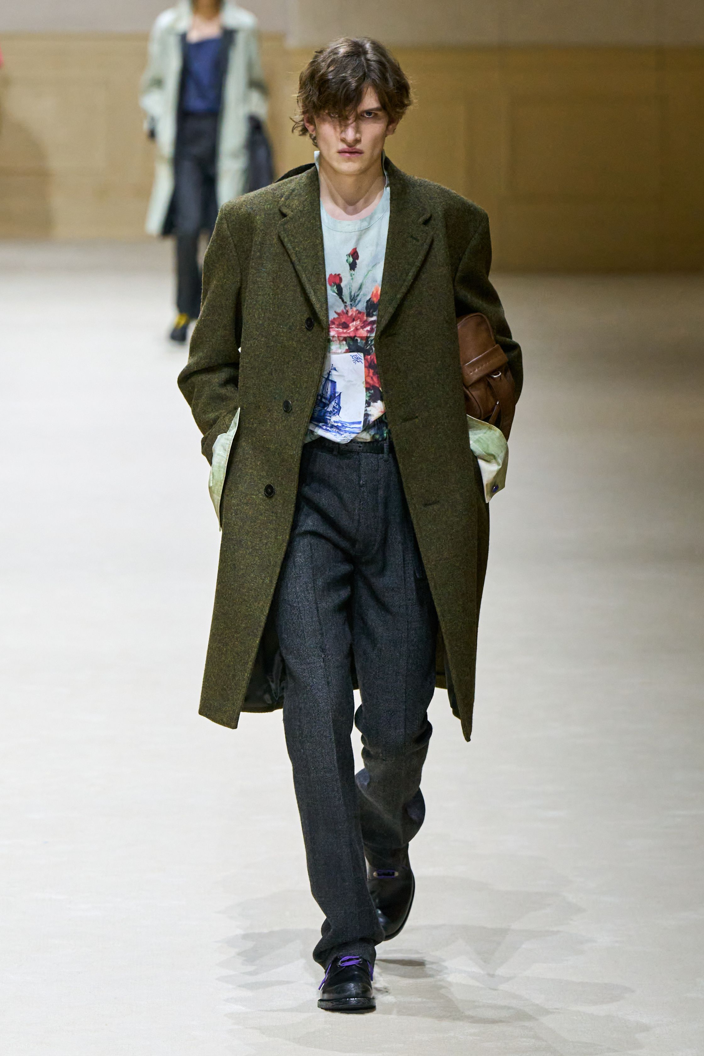 Prada 2026秋冬继续以“制服感”为切入口，重构男性权力与脆弱性的关系。修身西装、直筒大衣与功能性外套在高度理性的廓形中出现，却通过红色针织、围巾与内搭打破秩序。系列在严肃与松动之间反复摇摆，呈现一种当代男性在社会角色与个体情绪之间的张力。这是Prada一贯的冷静叙事，也是其思想性持续领先的关键简-顽石频道趋势研究
